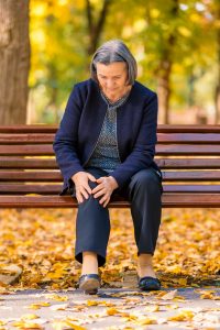 An older woman is having knee pain while sitting on a park bench..