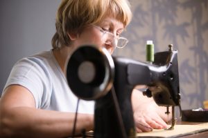 An older seamstress is sitting at a sewing machine. 