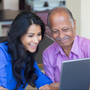 An older man and a younger woman smile while looking at a laptop screen together.